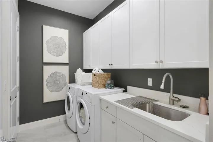 Laundry area with sink, washing machine and clothes dryer, cabinets, and light tile patterned flooring