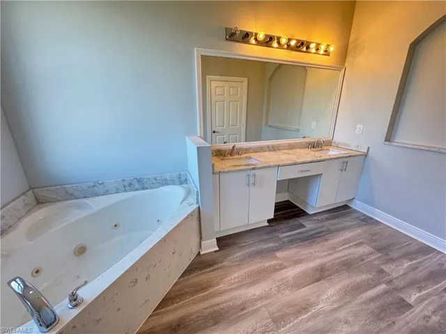 Bathroom with wood finished floors, double vanity, a tub with jets, and baseboards