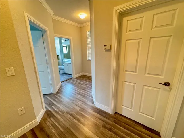 Hallway with ornamental molding, dark wood-style flooring, baseboards, and a textured wall