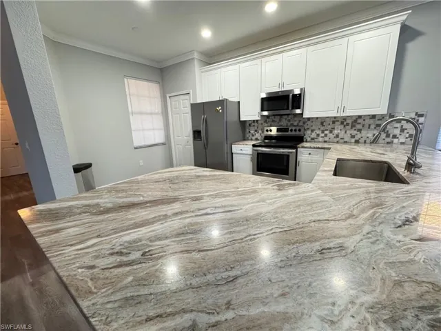 Kitchen featuring stainless steel appliances, a sink, light stone countertops, a peninsula, and ornamental molding
