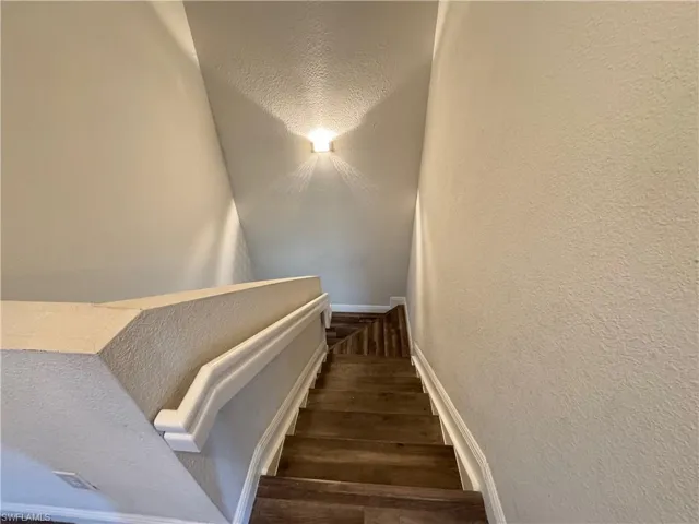 Stairway featuring wood finished floors, a textured wall, and baseboards