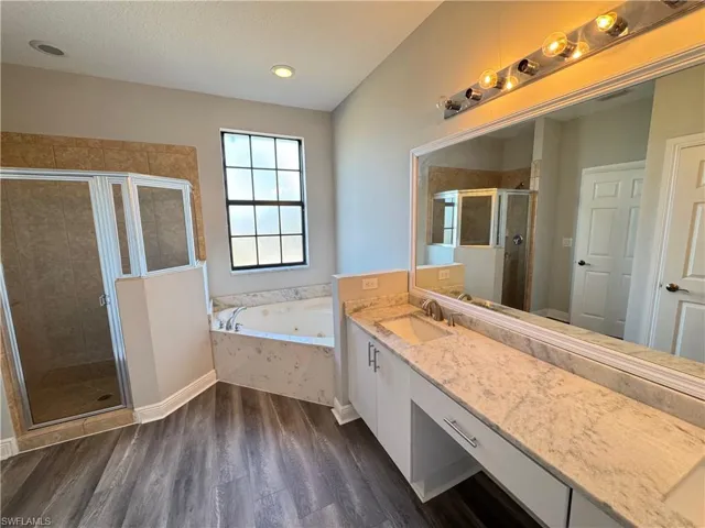 Full bath with a stall shower, wood finished floors, a jetted tub, vanity, and a textured ceiling