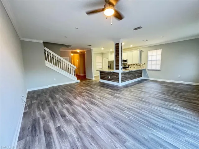 Unfurnished living room with crown molding, stairs, ceiling fan, baseboards, and dark wood finished floors