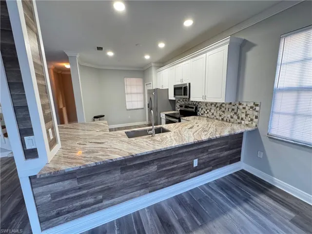 Kitchen with appliances with stainless steel finishes, crown molding, a sink, a peninsula, and light stone countertops