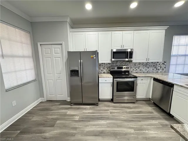 Kitchen with stainless steel appliances, crown molding, white cabinetry, backsplash, and light stone countertops