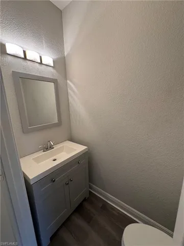 Bathroom with wood finished floors, vanity, toilet, baseboards, and a textured wall