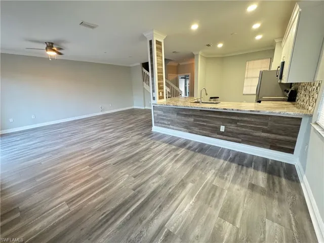 Kitchen with ornamental molding, wood finished floors, baseboards, light stone countertops, and a ceiling fan