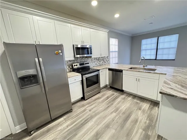 Kitchen with appliances with stainless steel finishes, a sink, ornamental molding, light wood-type flooring, and white cabinets