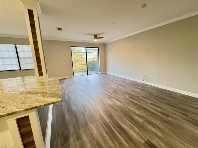 Unfurnished living room featuring a ceiling fan, ornamental molding, baseboards, and dark wood-style floors