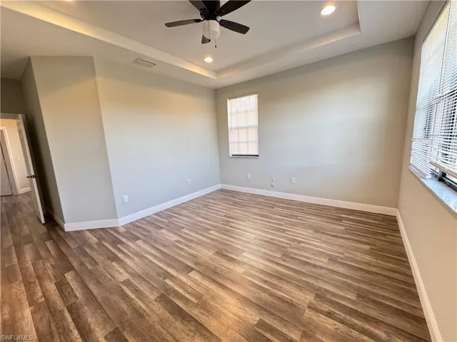 Unfurnished room with recessed lighting, a raised ceiling, ceiling fan, wood finished floors, and baseboards