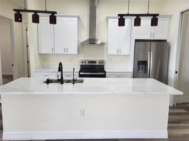 Kitchen with appliances with stainless steel finishes, wall chimney exhaust hood, an island with sink, dark wood finished floors, and white cabinets
