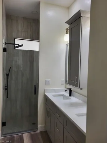 Full bath with double vanity, a shower stall, and wood finished floors