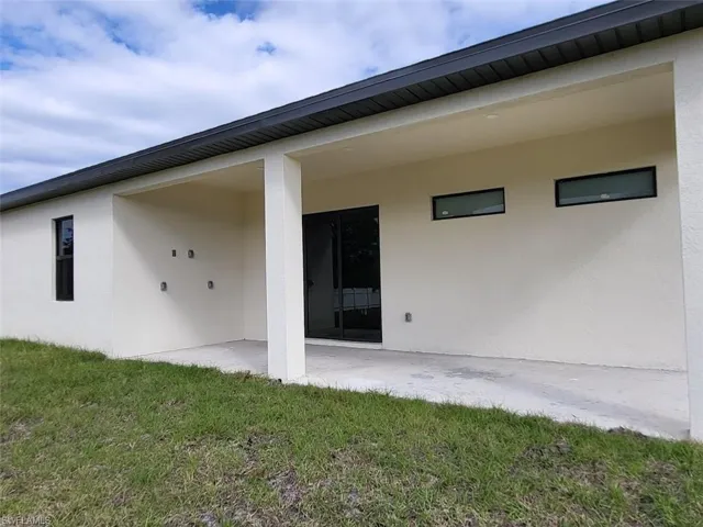 Rear view of property with a patio area, stucco siding, and a lawn