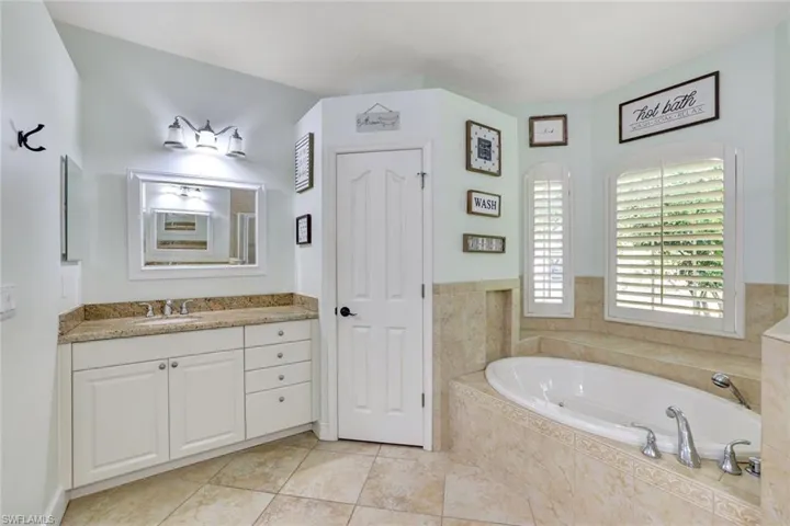 Bathroom featuring vanity, tile patterned flooring, and tiled bath