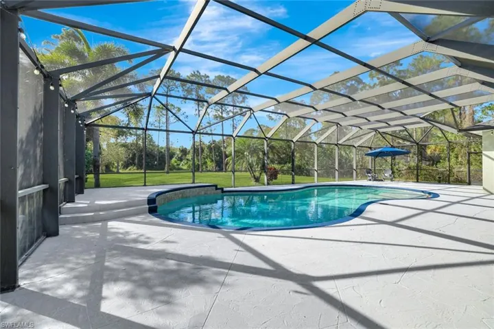 View of pool with a patio area, a lawn, and glass enclosure