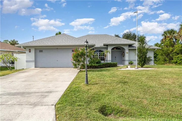 Ranch-style home with a shingled roof, a front lawn, an attached garage, driveway, and stucco siding