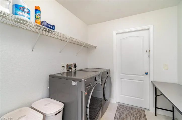 Laundry area featuring washing machine and clothes dryer, light tile patterned flooring, and a textured wall
