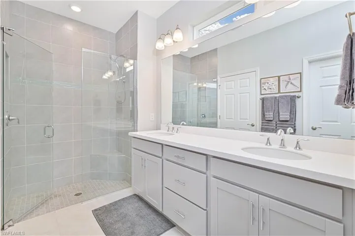 Bathroom featuring double vanity, a stall shower, and light tile patterned floors