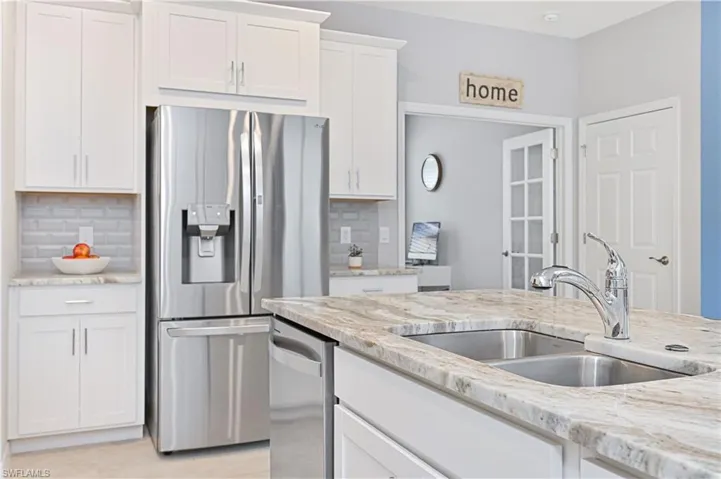 Kitchen with stainless steel appliances, white cabinetry, and light stone counters