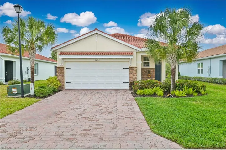 Mediterranean / spanish-style home featuring a front lawn, stone siding, a tiled roof, decorative driveway, and an attached garage