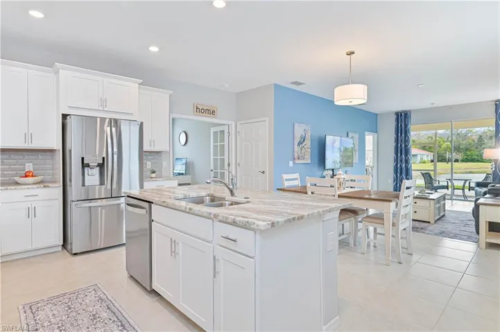 Kitchen featuring white cabinetry, pendant lighting, stainless steel appliances, light stone counters, and a center island with sink