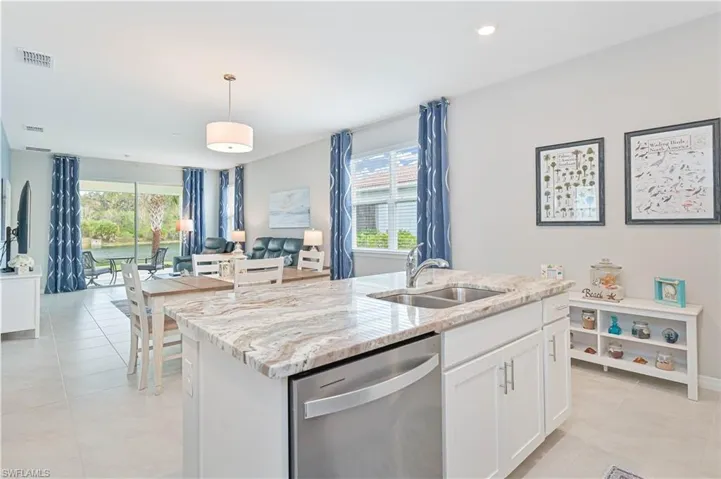 Kitchen with stainless steel dishwasher, white cabinets, light stone countertops, a kitchen island with sink, and open floor plan