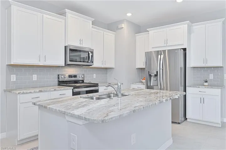 Kitchen featuring appliances with stainless steel finishes, light stone counters, decorative backsplash, an island with sink, and recessed lighting