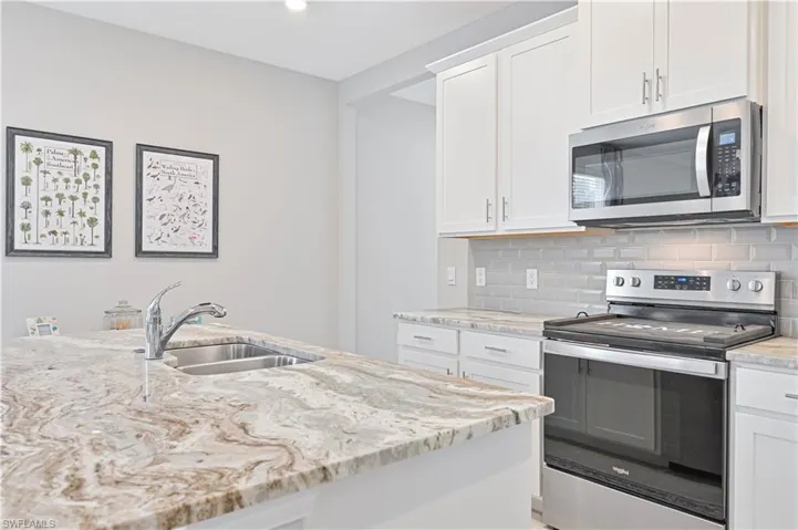 Kitchen featuring appliances with stainless steel finishes, white cabinetry, light stone counters, and tasteful backsplash