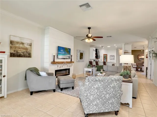 Living room featuring a ceiling fan, ornamental molding, a fireplace, and visible vents