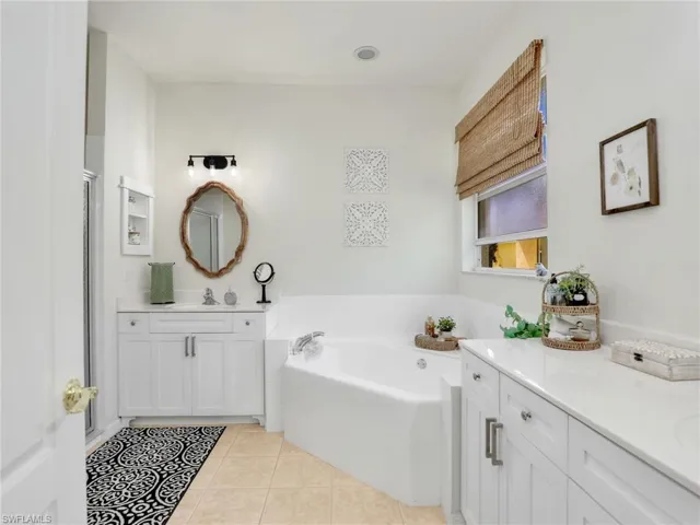 Full bath featuring tile patterned floors, a sink, two vanities, a shower with door, and a bath