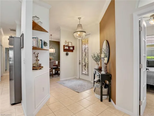 Entryway with ceiling fan with notable chandelier, light tile patterned floors, crown molding, and baseboards