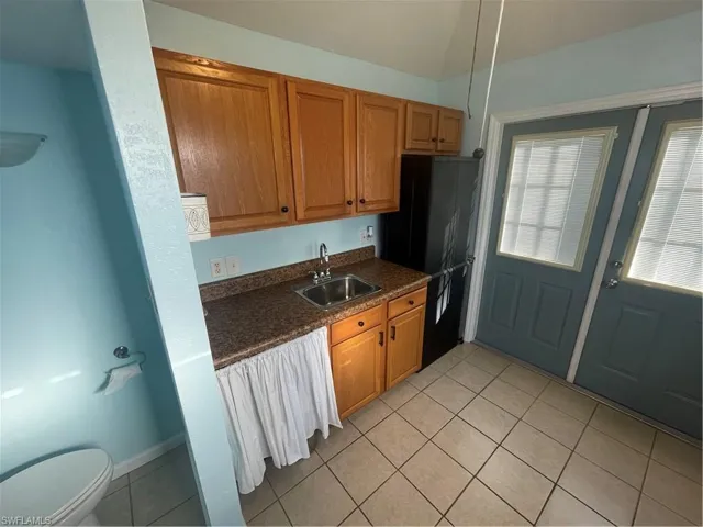 Kitchen featuring wood finish cabinetry, dark countertops, light tile patterned flooring, and refrigerator