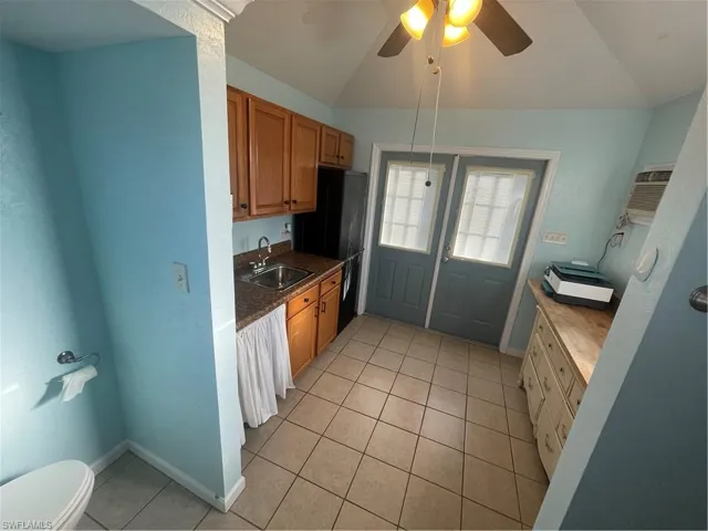 Kitchen with a ceiling fan, light tile patterned flooring, freestanding refrigerator, wood finish cabinets, and lofted ceiling