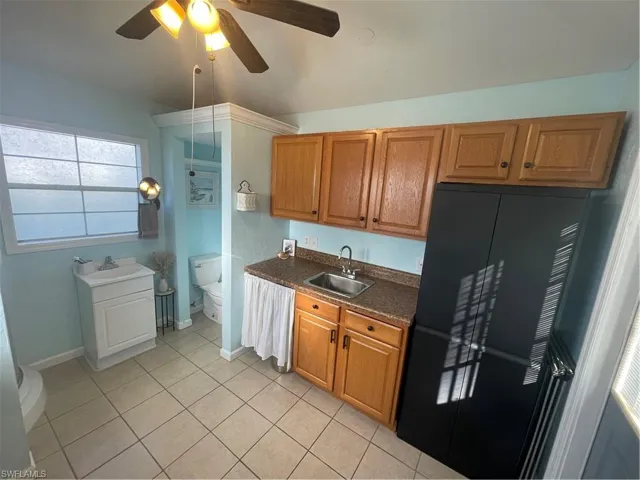 Kitchen with a ceiling fan, refrigerator, wood finish cabinets, and light tile patterned flooring