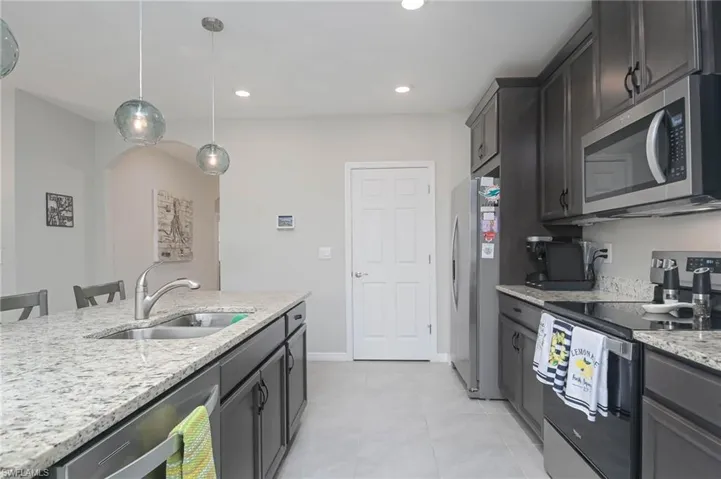 Kitchen featuring appliances with stainless steel finishes, a kitchen breakfast bar, light stone counters, decorative light fixtures, and sink