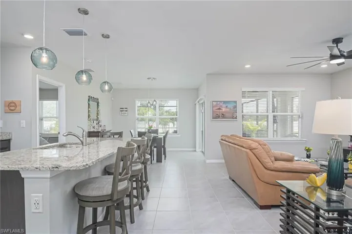 Kitchen with pendant lighting, sink, light tile patterned floors, light stone countertops, and ceiling fan