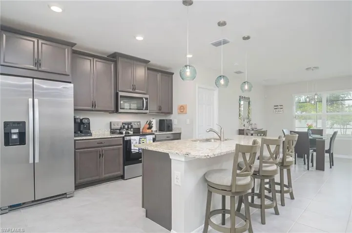 Kitchen featuring sink, decorative light fixtures, a center island with sink, appliances with stainless steel finishes, and light stone countertops