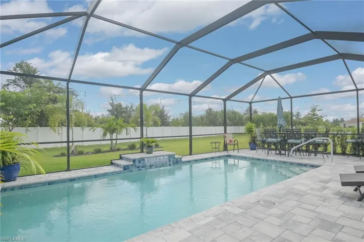 View of swimming pool with pool water feature, glass enclosure, a patio area, and a lawn