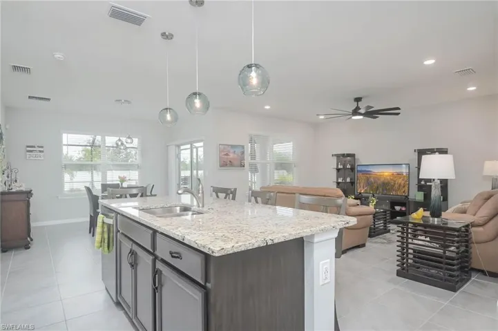 Kitchen with light stone counters, sink, hanging light fixtures, a center island with sink, and ceiling fan