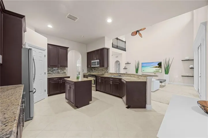 Kitchen with a kitchen island, appliances with stainless steel finishes, dark brown cabinets, light stone counters, and tasteful backsplash