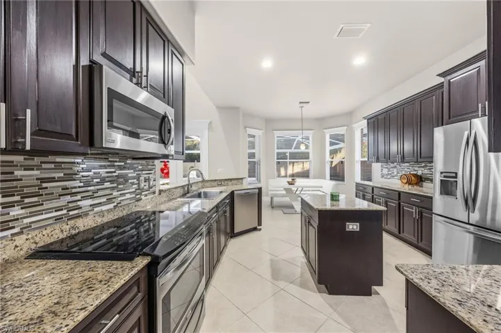 Kitchen featuring stainless steel appliances, a center island, hanging light fixtures, dark brown cabinetry, and light stone countertops
