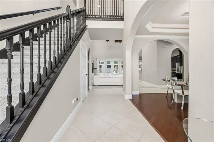 Entryway featuring light tile patterned flooring, crown molding, arched walkways, a towering ceiling, and a tray ceiling