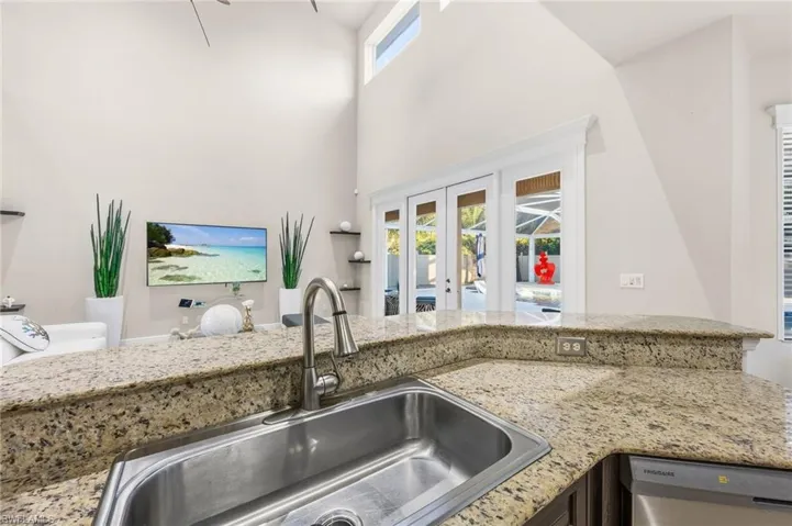 Kitchen featuring light stone countertops, healthy amount of natural light, dishwasher, french doors, and a high ceiling