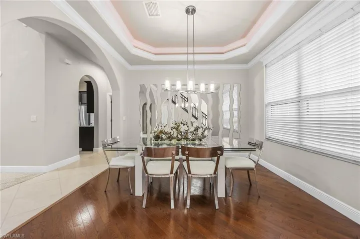 Dining area with ornamental molding, wood-type flooring, a chandelier, arched walkways, and a raised ceiling