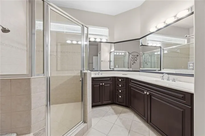 Bathroom with double vanity, a shower stall, light tile patterned floors, and healthy amount of natural light