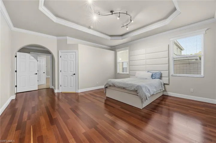 Bedroom featuring arched walkways, dark wood-style flooring, ornamental molding, and a tray ceiling