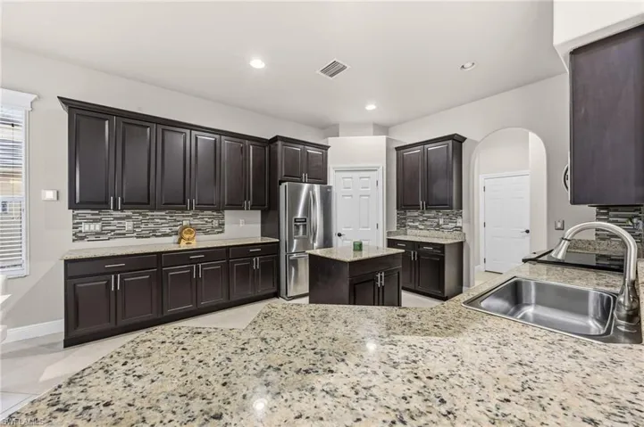 Kitchen featuring arched walkways, stainless steel fridge, a center island, light stone countertops, and backsplash