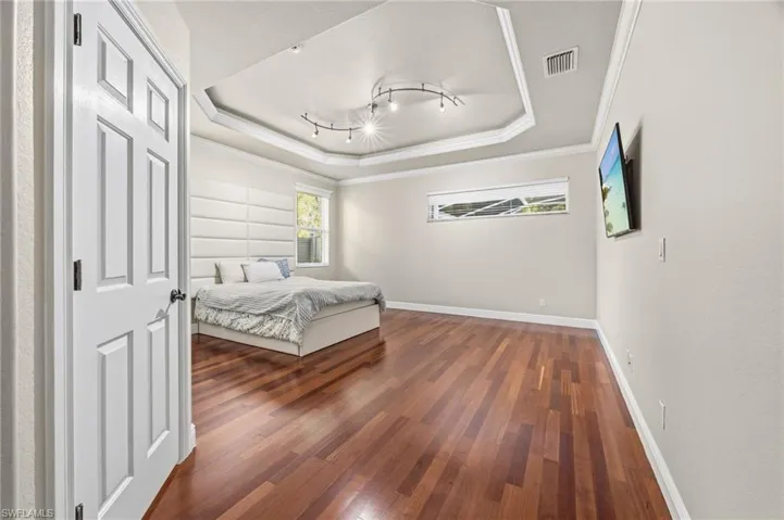Bedroom with crown molding, dark wood-style flooring, a raised ceiling, and track lighting