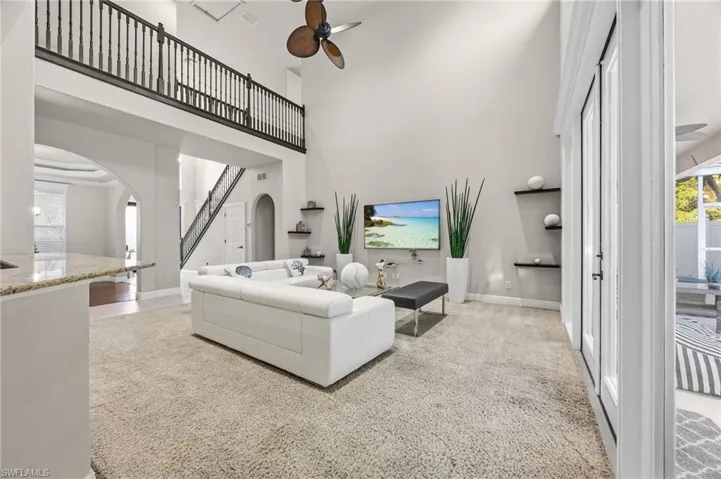 Living room with ceiling fan, plenty of natural light, light colored carpet, a towering ceiling, and arched walkways