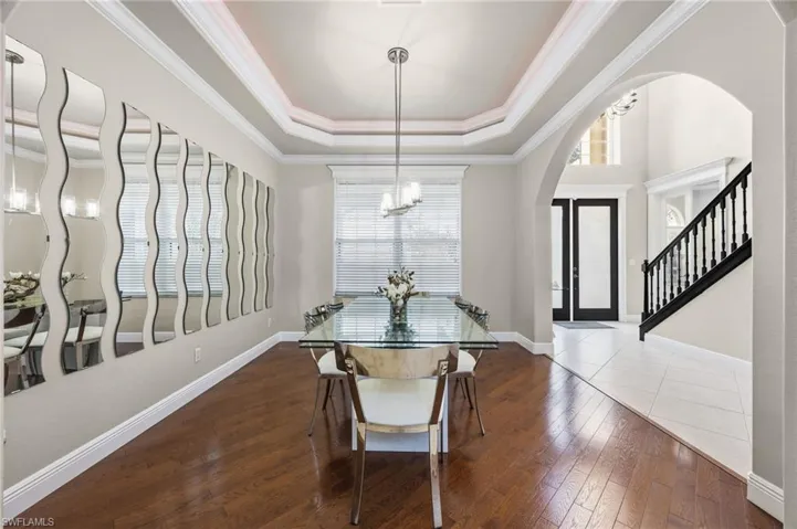 Dining space featuring dark wood-type flooring, arched walkways, crown molding, a chandelier, and a raised ceiling